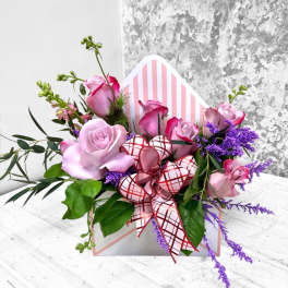 Pink roses in a striped gift box with a red plaid ribbon
