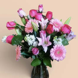 Pink roses and gerbera daisies arranged in a dark glass vase
