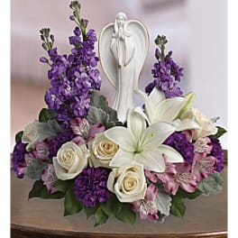Purple and white floral arrangement with a praying angel figurine