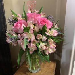 Pink roses and alstroemeria in a glass vase with a heart pick