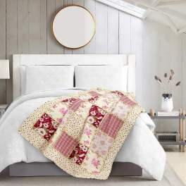 Patchwork quilt draped over a white bed in a bright bedroom