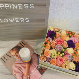 Box of pastel roses with a candle and magazine beside a flower sign