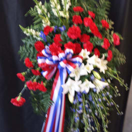 Standing floral spray with red carnations, white lilies, and a red-white-blue ribbon
