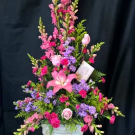 Tall pink and purple floral arrangement in a white pedestal vase