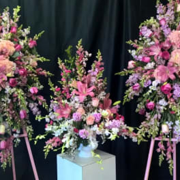 Three pink and lavender floral arrangements on stands and a pedestal