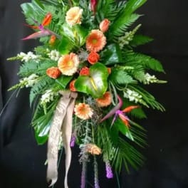 Tall tropical standing spray with orange and peach flowers on a black easel