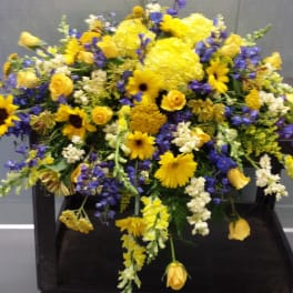 Large yellow and blue floral arrangement on a dark stand
