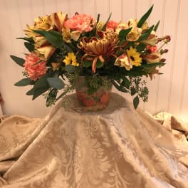 Mixed bouquet in a decorative vase with yellow, coral, and burgundy flowers