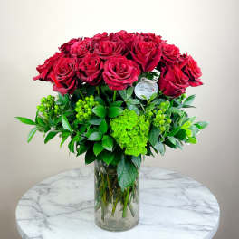 Red roses arranged in a clear glass vase with bright green foliage