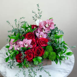 Red roses and pink orchids in a low rectangular arrangement with greenery