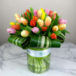 Colorful tulip bouquet in a glass vase with striped leaf wrap