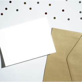 Blank white card beside a gold envelope on a confetti background