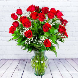 Red roses arranged in a clear glass vase with white filler flowers