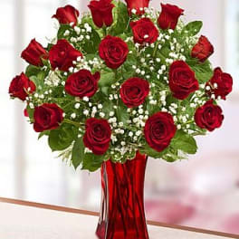 Red roses in a red glass vase with white filler flowers