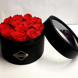 Red roses arranged in a black round box with a clear lid
