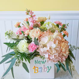 Pastel flower arrangement in a white vase with "New Baby" text