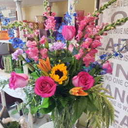 Mixed bouquet of pink roses, sunflowers, and blue flowers in a glass vase