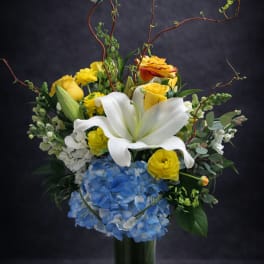 Bouquet of white lilies, yellow roses, and blue hydrangea in a glass vase