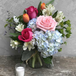 Bouquet of pink and orange roses with blue hydrangeas in a glass vase