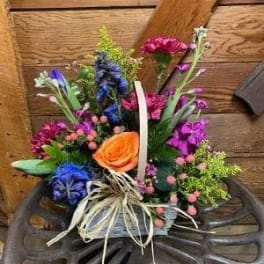 Colorful mixed bouquet with an orange rose and blue flowers in a basket