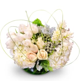 Cream roses and white flowers in a green glass bowl with looping grass stems