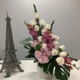 Pink and white floral arrangement in a white vase beside a small Eiffel Tower model