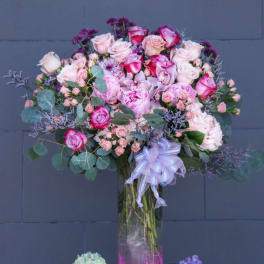 Tall bouquet of pink and lavender roses in a glass vase with a ribbon