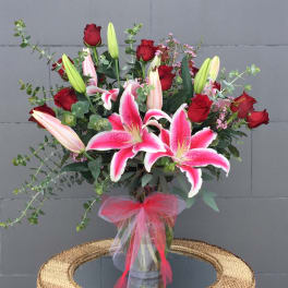 Bouquet of pink lilies and red roses in a glass vase with a pink ribbon
