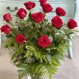 Red roses arranged in a clear glass vase with fern foliage
