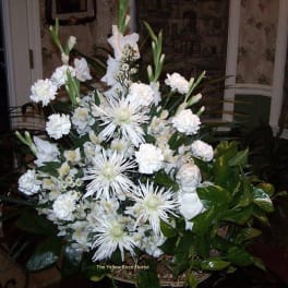 Large white floral arrangement in a basket with a small angel figurine
