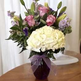 Pink roses and white hydrangeas in a purple vase with a ribbon