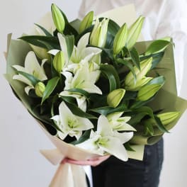 Bouquet of white lilies with green buds wrapped in pale paper