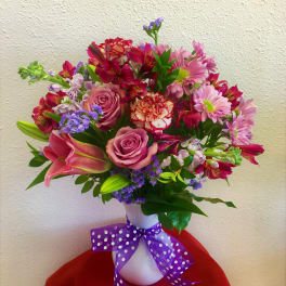 Mixed bouquet of pink and purple flowers in a white vase with a purple ribbon