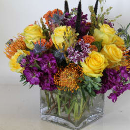Bouquet of yellow roses and purple flowers in a clear square vase