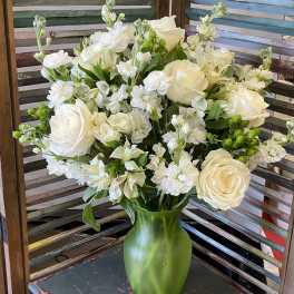 White roses and small white flowers arranged in a green vase