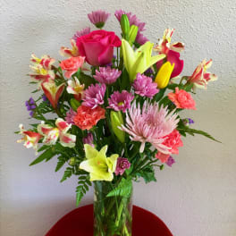 Mixed bouquet in a clear glass vase with pink roses, lilies, and daisies