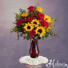 Bouquet of red roses and yellow sunflowers in a burgundy glass vase