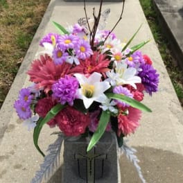 Colorful floral arrangement with daisies, lilies, and pink blooms in a cemetery vase