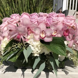 Pink roses and orchids arranged in a low rectangular vase