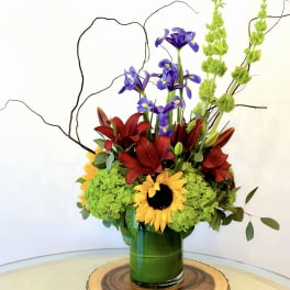 Colorful floral arrangement with sunflowers, red lilies, and purple irises in a green vase
