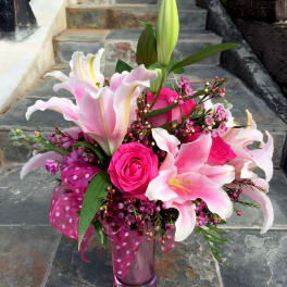 Pink lilies and roses arranged in a glass vase with a polka-dot ribbon.