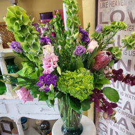 Tall mixed bouquet in a glass vase with green hydrangeas, purple blooms, and pink flowers