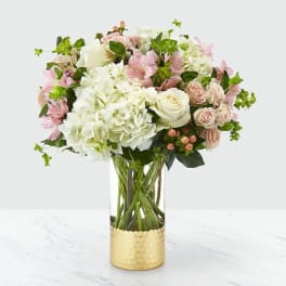 Pink and white flowers arranged in a clear glass vase with a gold base
