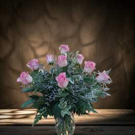 Pink roses arranged in a clear glass vase with mixed greenery