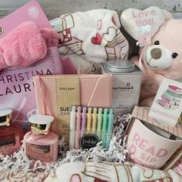 Pink gift basket with a teddy bear, candles, book, and stationery items