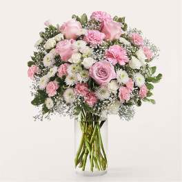 Pink and white bouquet of roses, carnations, and daisies in a clear glass vase
