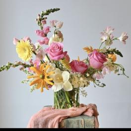 Mixed bouquet of pink roses, yellow daisies, and white flowers in a glass vase