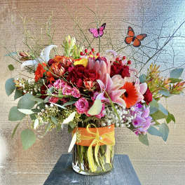 Colorful mixed flower arrangement in a glass vase with butterfly picks