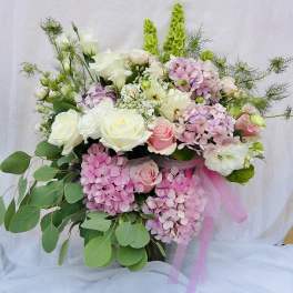 Bouquet of pink and white roses with hydrangeas and greenery, tied with pink ribbon