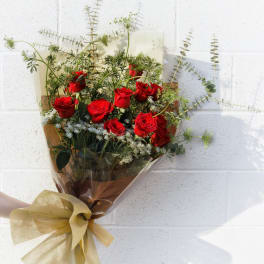 Bouquet of red roses with airy greenery wrapped in brown paper and gold ribbon